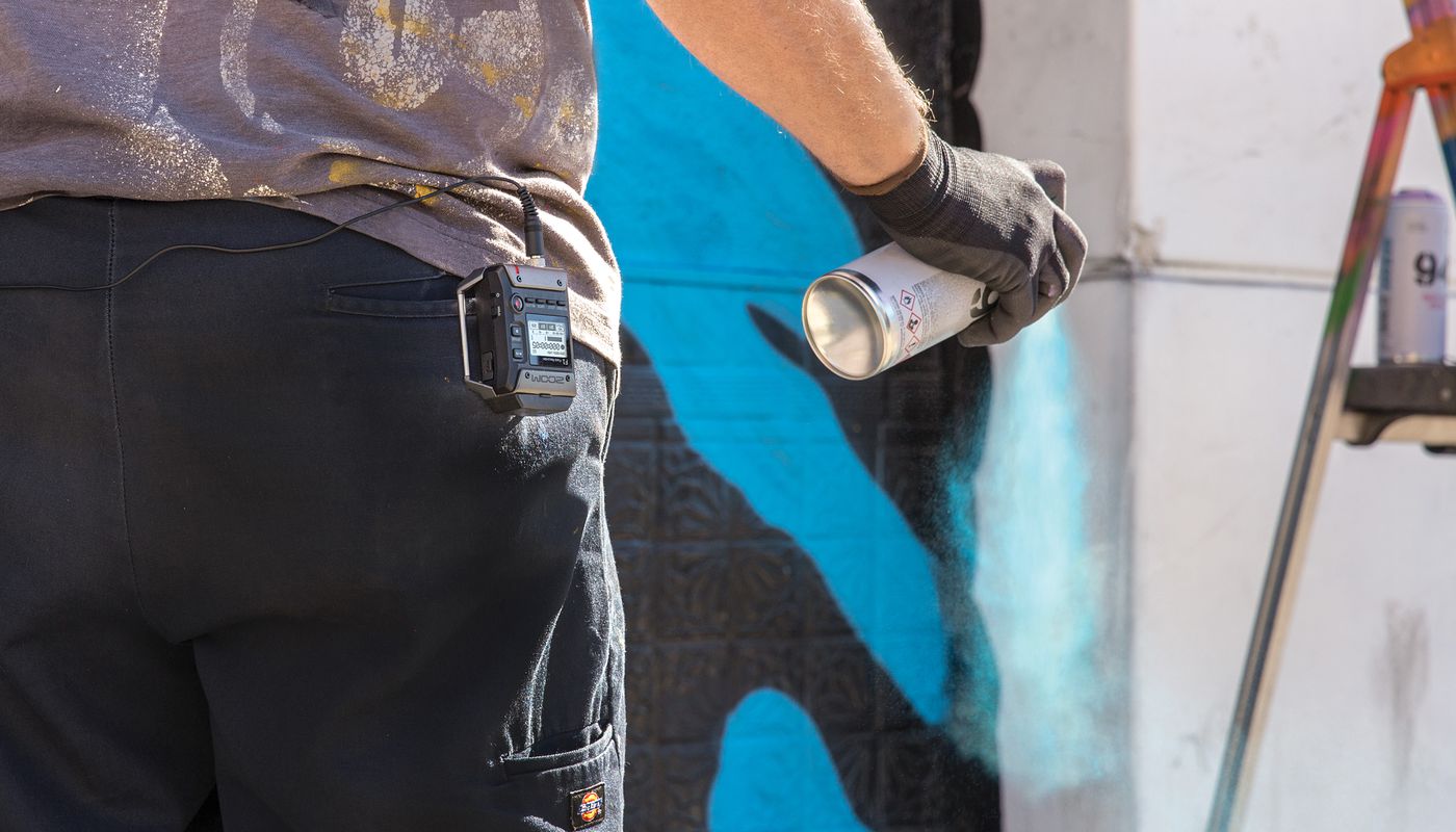 Street artist using spray paint to create his artwork, with F1 connected to his belt