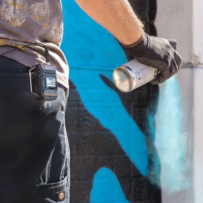 Street artist using spray paint to create his artwork, with F1 connected to his belt