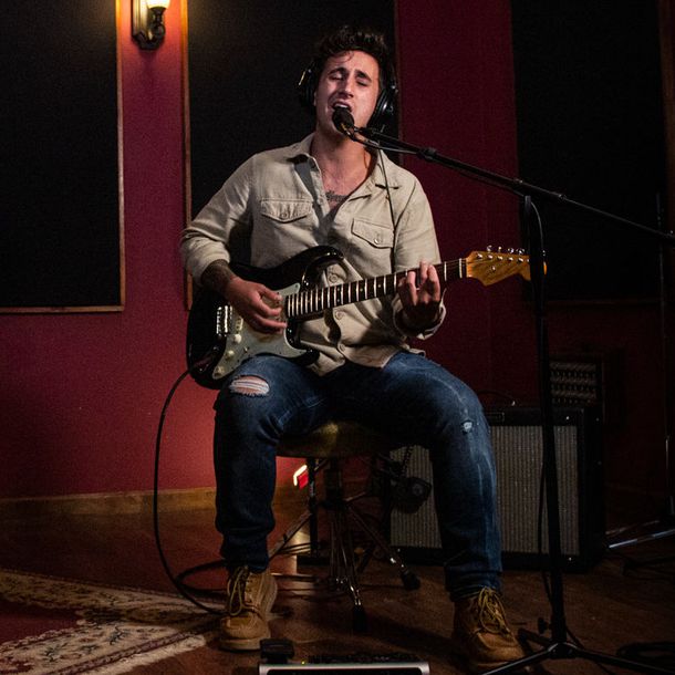 Aaron Rizzo Sitting singing with guitar