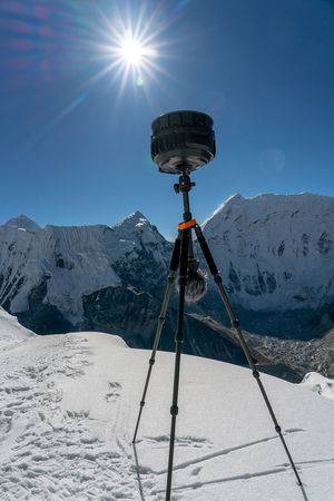 portrait oriented view of f6 on tripod on in snow with sun shining in background sky above mountains