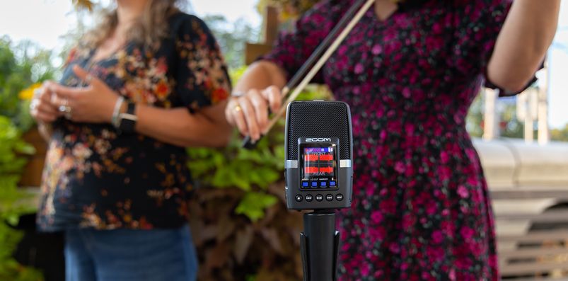 Several musicians standing around an H2essential mounted on a microphone stand, recording their performances